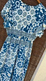 Vestido largo de seda con estampado floral en tonos azules y beige, escote en V, mangas cortas con volados y falda con volados escalonados.