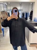 Camisa negra con pequeños brillos, de corte oversize y mangas largas con puños abotonados.