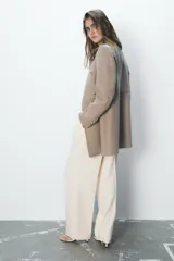 Abrigo color beige confeccionado en lana. Tiene cuello subido, mangas largas con hombreras, forro interior combinado y cierre frontal cruzado con botones metálicos.