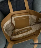 Bolso tipo tote de cuero color beige con textura granulada y tachas plateadas en los laterales.