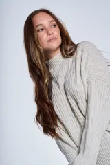 Sweater color crema de punto trenzado, con cuello alto y mangas largas.