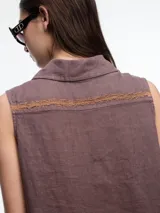 Camisa sin mangas negra de lino con cuello clásico, cierre frontal abotonado y bolsillo de parche en el pecho. Presenta bordados tipo pespunte en contraste en el frente y canesú trasero.