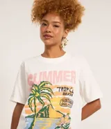 Remera de algodón color blanco, de corte alargado, con cuello redondo y manga corta. Presenta una estampa frontal de estilo tropical con palmeras, flores y texto 'Summer Tropical Beach'.