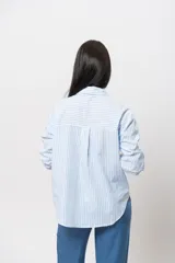 Camisa celeste a rayas verticales blancas, de corte recto y mangas largas con puños abotonados.