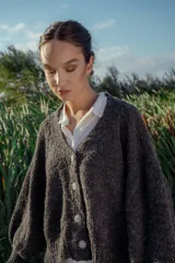 Cárdigan tejido de boucle color gris oscuro, con escote en V, mangas largas abullonadas y cierre frontal con botones grandes. Corte holgado.