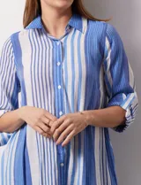 Camisa larga de rayón marca Robert Louis, con estampado a rayas verticales en tonos coral y blanco. Tiene cuello con solapa, abertura central con botones, mangas largas regulables con presilla y botón, y tajos laterales.