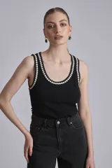 Remera negra ajustada al cuerpo, tipo musculosa, con escote redondo y ribetes en blanco con apliques de perlas en el contorno del cuello y las sisas.