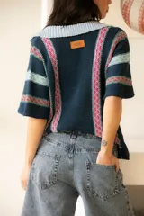 Camisa tejida de algodón a rayas verticales en tonos azul, celeste y rosa, con botones al frente y mangas cortas.