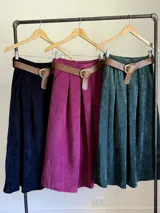 Falda midi de corderoy color beige claro, con pliegues verticales marcados y cintura elastizada. Incluye un cinturón desmontable de cuero marrón con hebilla dorada.