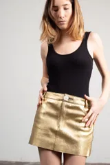 Falda corta de cuero color dorado con textura craquelada y cierre frontal con botón blanco.