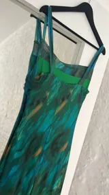 Vestido largo ajustado al cuerpo, confeccionado en microtul estampado con diseño abstracto en tonos verde, azul y marrón. Tiene breteles finos y forro interior opaco.