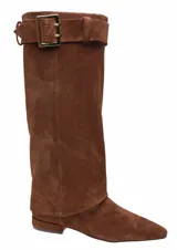 Bota de caña alta confeccionada en cuero gamuza color marrón. Presenta un diseño de caña ancha con efecto polaina que cae sobre el pie, punta fina y detalle de correa con hebilla metálica dorada en el borde superior.