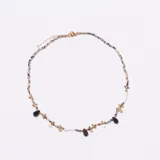 Gargantilla corta con cadena de pequeñas cuentas jaspeadas en tonos blanco y negro, y detalles dorados. Presenta colgantes de piedras negras en forma de gota y pequeños discos dorados.