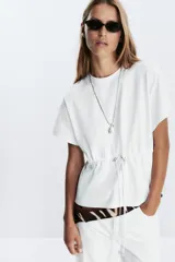 Camiseta color crudo de algodón con cuello redondo, manga corta caída y cintura ajustable con cordón.