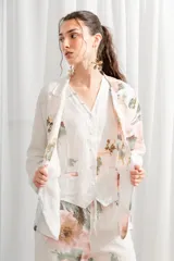 Blazer de lino blanco con estampado floral en tonos rosa y verde, corte holgado, cuello solapa y bolsillos laterales.