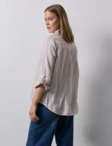 Camisa color beige con rayas verticales blancas, de lino, con cuello con solapa y abertura central con botones. Tiene un bolsillo aplicado en el pecho y mangas largas regulables con presilla y botón.