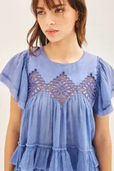 Camisa azul de algodón liviano con cuello redondo y gota en la espalda. Presenta detalle de bordado calado, terminación de volado en mangas y ruedo.