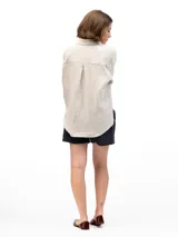 Camisa de lino beige de manga larga, corte clásico y holgado, con cuello camisero y cierre frontal con botones.