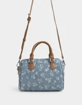 Cartera bowling de denim celeste con estampado de flores blancas, doble asa corta de cuero marrón y correa larga regulable y desmontable.