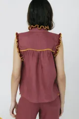 Blusa color borgoña con cuello alto y mangas cortas, con detalle de volados tejidos en color mostaza en cuello, mangas y bolsillos.