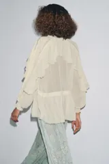 Blusa color crudo confeccionada en viscosa, con cuello redondo, escote en pico, mangas largas con puños elásticos, volantes frontales y detalles de encaje.