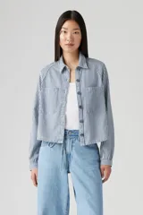 Camisa a rayas verticales azules y blancas, con cuello clásico, cierre frontal con botones y dos bolsillos de parche en el pecho.