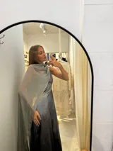 Vestido largo de tafeta con brillo, color gris o plateado, con escote asimétrico de un solo hombro y una pieza de seda liviana que cae como una capa o chal.