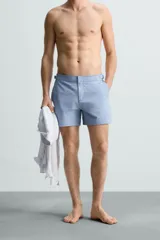 Short de baño celeste de tejido técnico con cintura elástica ajustable con cordón interior y trabillas laterales. Tiene bolsillos frontales y bolsillo trasero con cierre de cremallera. Cuenta con forro interior y cierre frontal con cremallera y botón a presión oculto.