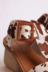Sandalias planas con tiras de cuero con estampado de vaca en blanco y negro, y hebilla lateral.