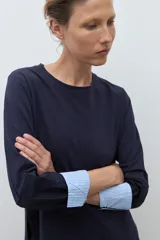 Remera de manga larga color azul marino con cuello redondo. Los puños de las mangas son doblados y revelan un forro de tela a rayas finas blancas y celestes.