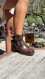 Botas cortas de cuero color marrón oscuro con hebillas y estribo desmontable.