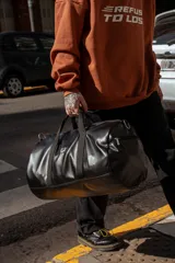 Bolso duffel negro de cuero sintético con logo de ancla bordado en rosa. Tiene doble asa de mano reforzada, correa de hombro regulable y desmontable, cierre superior con doble cremallera y tres bolsillos (dos exteriores y uno interior).