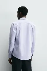 Camisa celeste a rayas verticales blancas, de corte recto, con cuello italiano abierto, mangas largas con puños abotonados y cierre frontal con botones.
