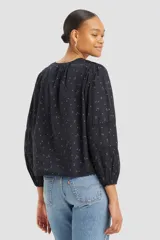 Blusa negra de algodón con estampado floral, cuello redondo con abertura y botones, mangas largas abullonadas con detalles de encaje y corte holgado.