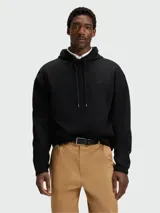 Buzo negro con capucha y cordones ajustables, corte holgado y pequeño logo bordado en el pecho. Se lleva sobre una camisa blanca de cuello.