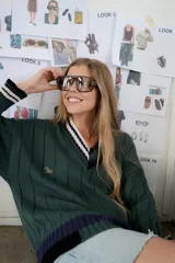 Buzo tejido verde con escote en V, cuello con rayas blancas y azul marino, y puños y ruedo con detalle de rayas.