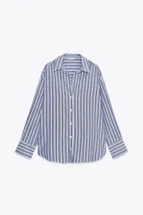 Camisa de algodón a rayas verticales azules y blancas con hilo metalizado, cuello solapa y escote pico. Manga larga acabada en puño, bajo asimétrico y cierre frontal con botones.