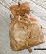 Mochila de cuero color camel con solapa con flecos y cierre con cordón de cuero.
