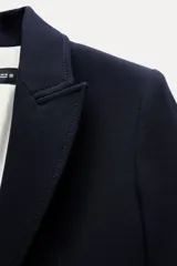 Blazer negra entallada con cuello solapa, manga larga con hombreras, bolsillos delanteros con solapa y cierre frontal con botones dorados.