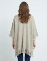 Kimono tejido en punto suave, color beige y crudo, con diseño de espiga (herringbone). Presenta mangas amplias, bolsillos frontales y terminación con flecos en el ruedo.