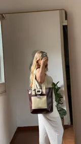 Bolso tote de ecocuero marrón oscuro con textura cocodrilo y un parche frontal de cuero liso marrón claro. Posee asas de hombro de cuero marrón y un broche decorativo blanco en el frente.