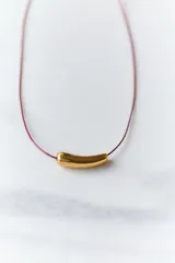 Gargantilla con tiento de hilo encerado color borgoña y dije de acero quirúrgico hipoalergénico plateado en forma de tubo.