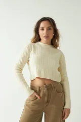 Sweater corto color crema con diseño trenzado, cuello redondo y mangas largas.