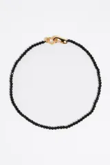 Collar de cuentas de cristal facetado color negro, con cierre de mosquetón dorado y dije de corazón dorado.