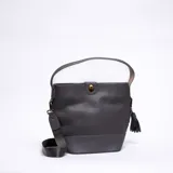 Cartera tipo bucket color gris oscuro, con correa de mano y correa bandolera ajustable. Cierre con broche metálico y detalle de borla lateral.