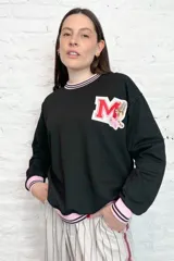 Buzo negro de corte suelto con detalles en rosa y parche con letra en el pecho.