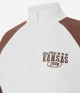Saco femenino de poliviscosa, color blanco con mangas raglán marrones y ribetes blancos. Tiene cuello alto, cierre frontal de cremallera y bordado lettering "Kansas City" en el pecho.