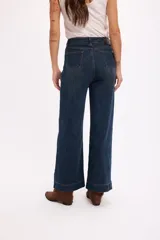 Pantalón de jean azul oscuro de tiro alto, con costuras verticales decorativas en el frente y cierre de botón metálico.