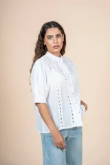 Blusa blanca con detalles bordados en toda la superficie, cuello levemente subido y botones al frente.