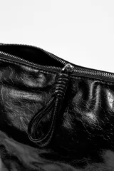 Bandolera negra de cuero sintético con correa de hombro ajustable y cierre superior con cremallera.